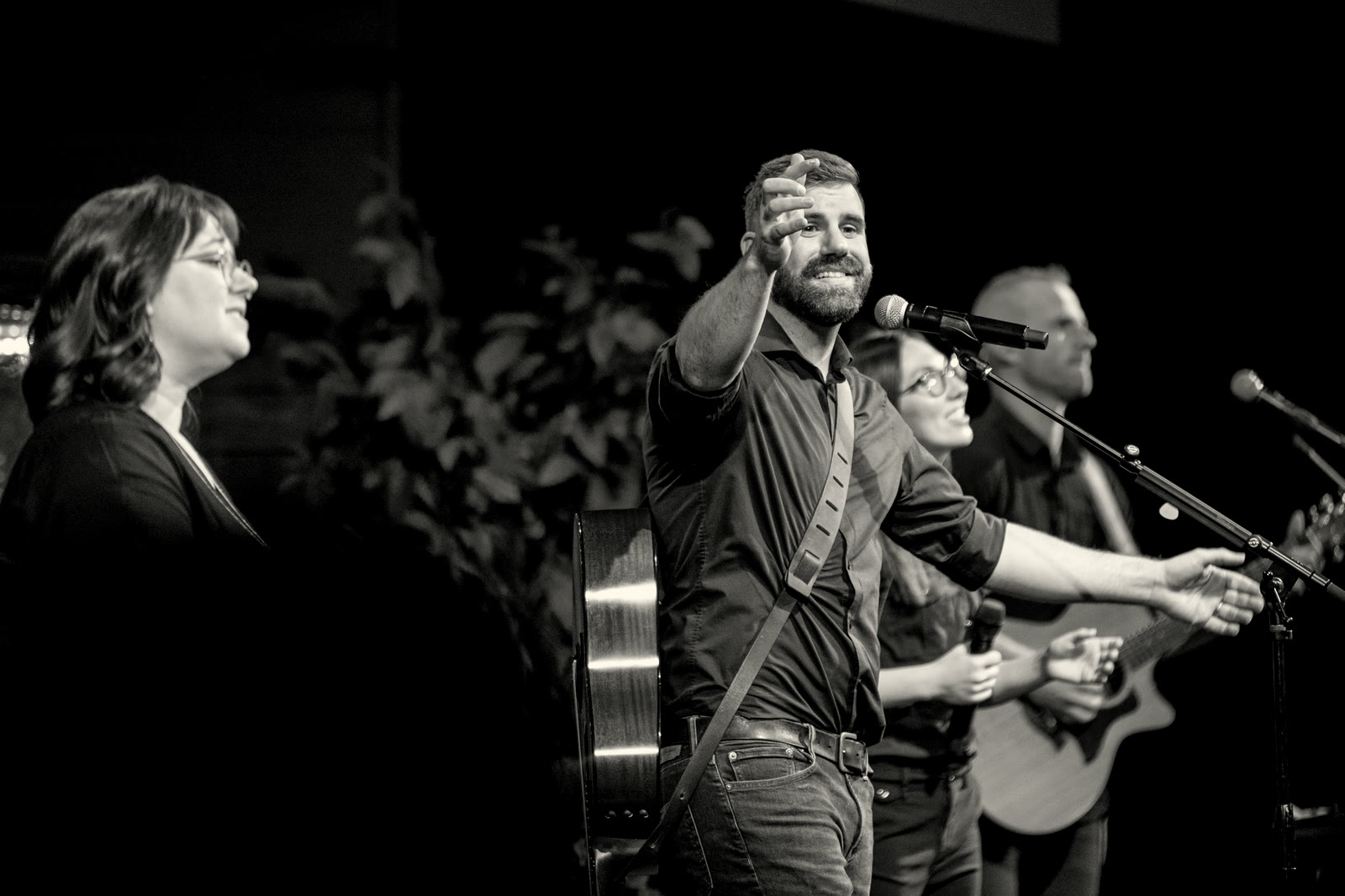 Casey Klocek on stage with singers and a guitarist, reaching out toward the room